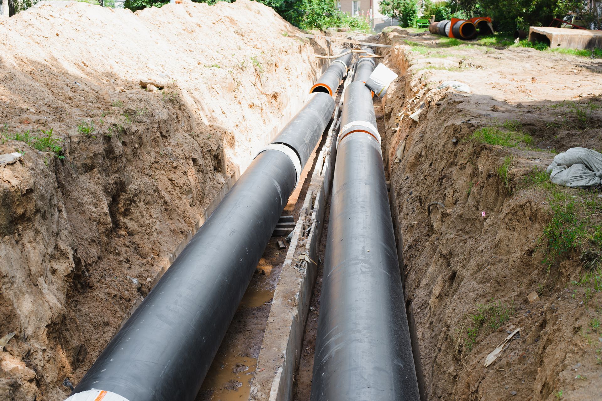 Two black pipes are being installed in a trench.