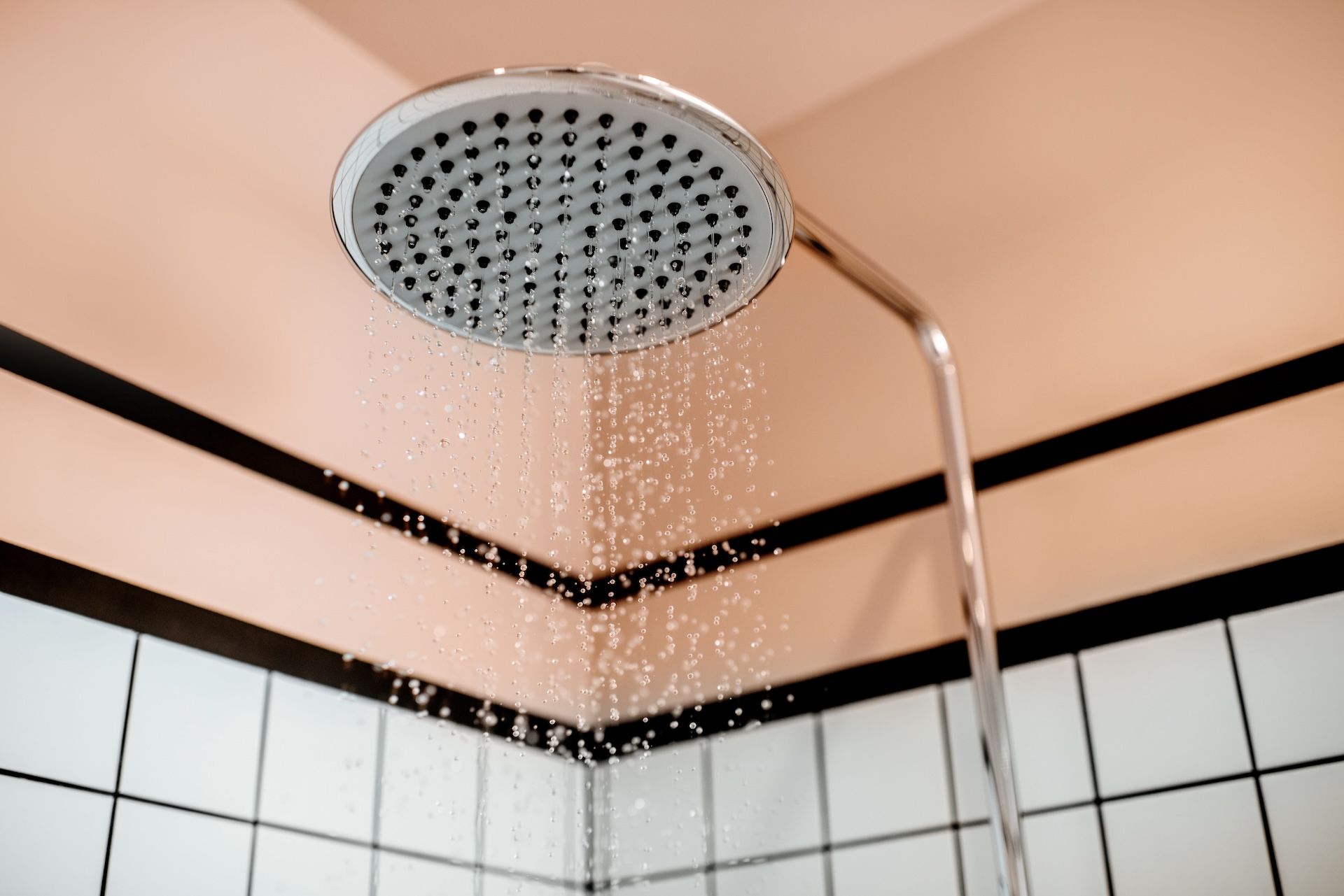 Showerhead dispensing water; white tile, black trim, and pink wall visible.
