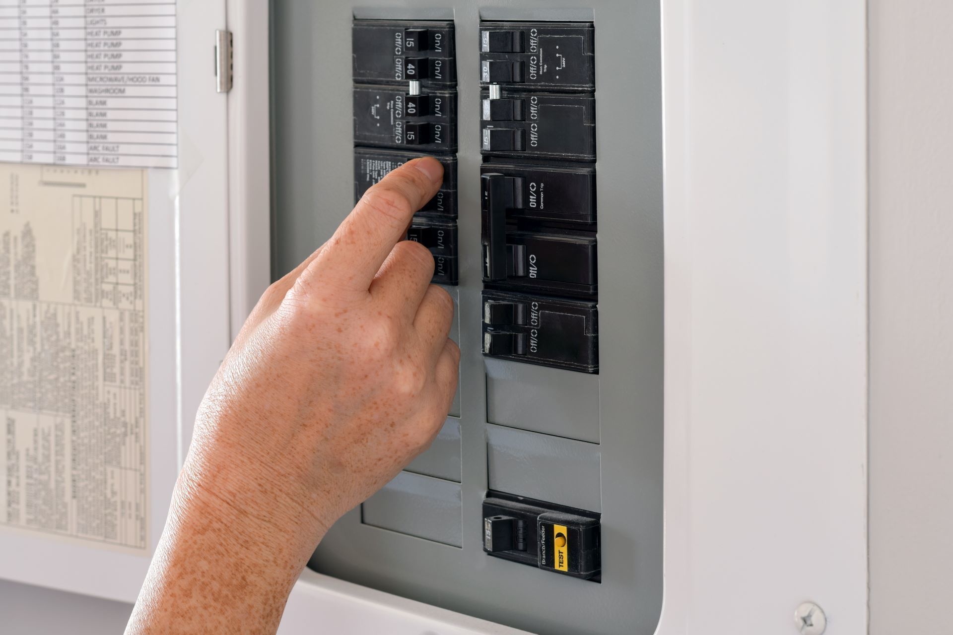 A hand flipping a black circuit breaker switch inside an electrical service panel.
