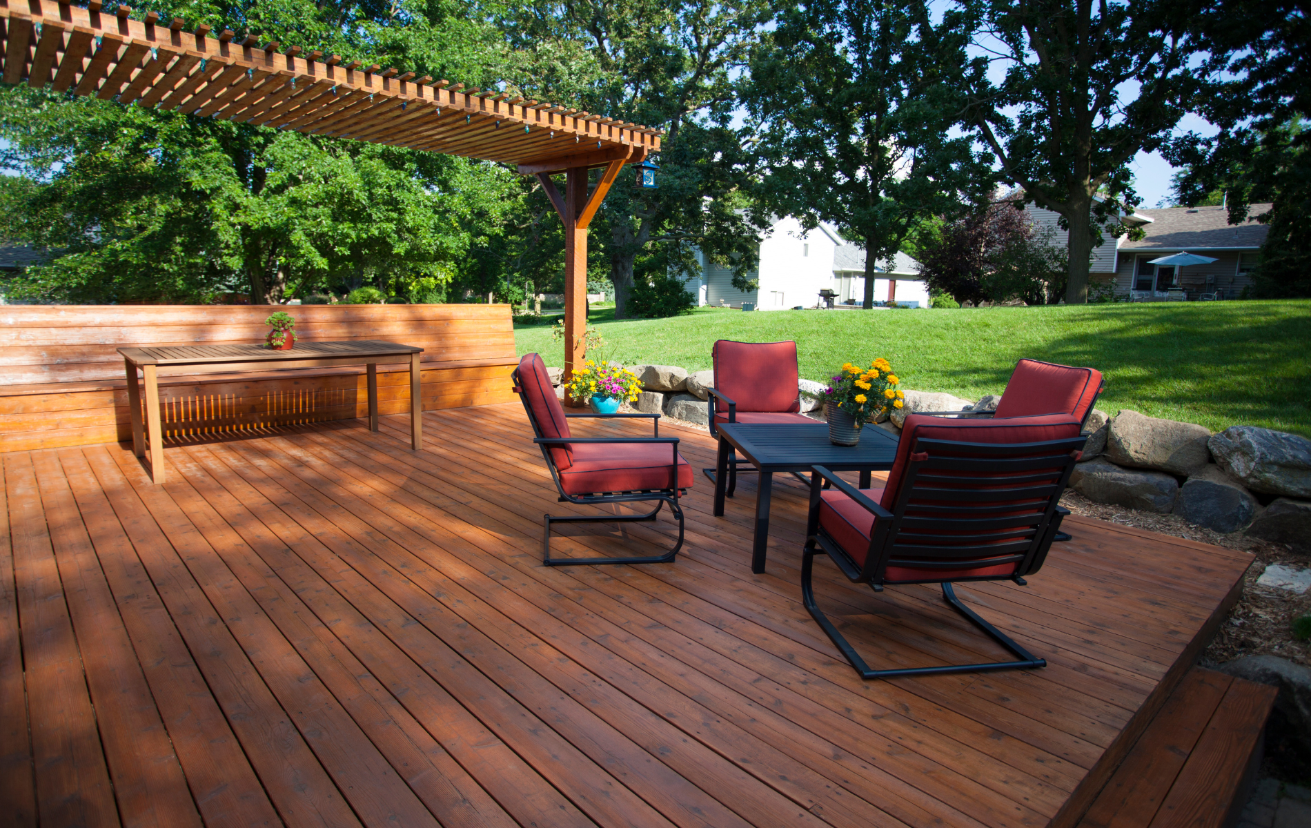Wooden deck with seating under a pergola, overlooking a grassy yard.