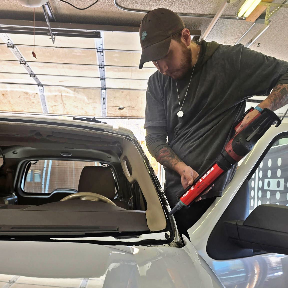 Person using a red power tool to work on a car windshield in a garage