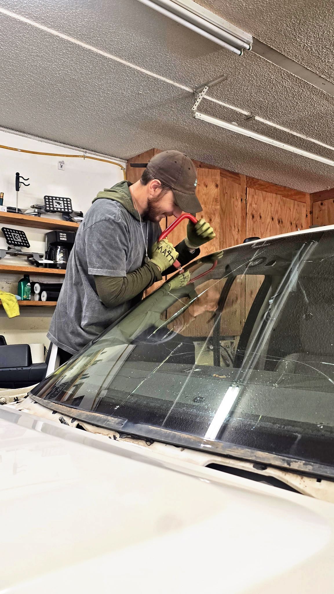 Person cleaning a car windshield in a garage with a yellow cloth