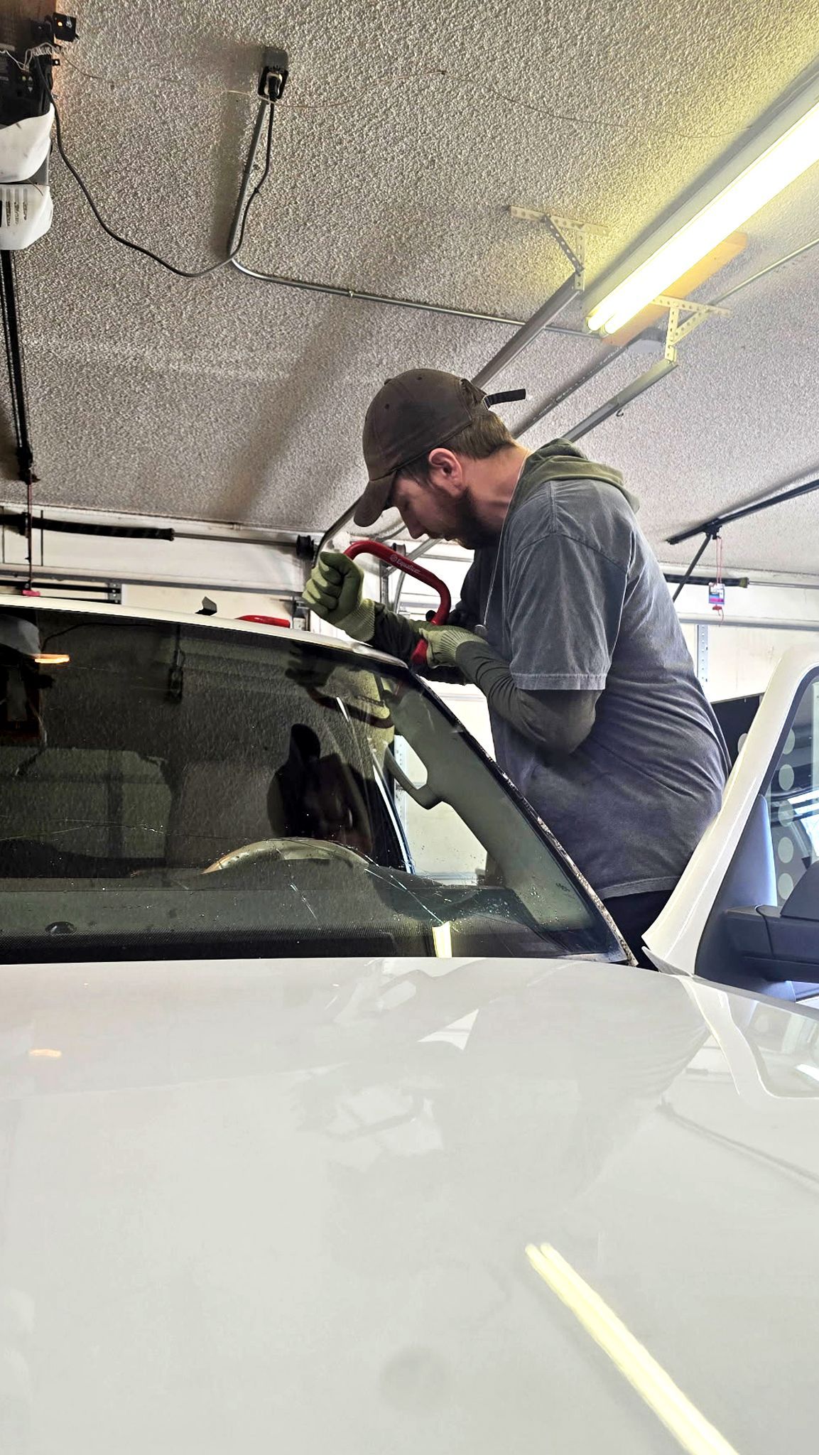 Mechanic inspecting the windshield of a white car inside a garage, under bright fluorescent lights