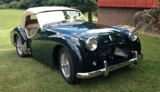 Dark green classic Triumph TR3 convertible parked on grass.
