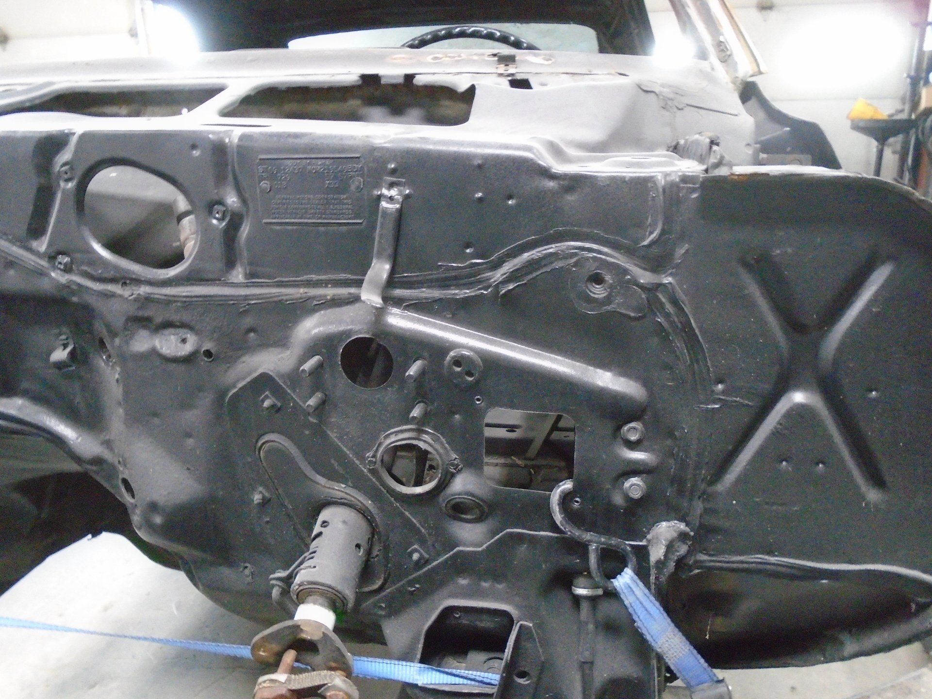 Black car engine bay with various holes and brackets, restoration process.