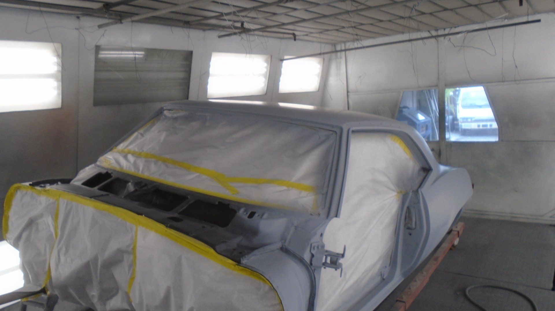 Car in primer stage, masked for painting, inside a spray booth.