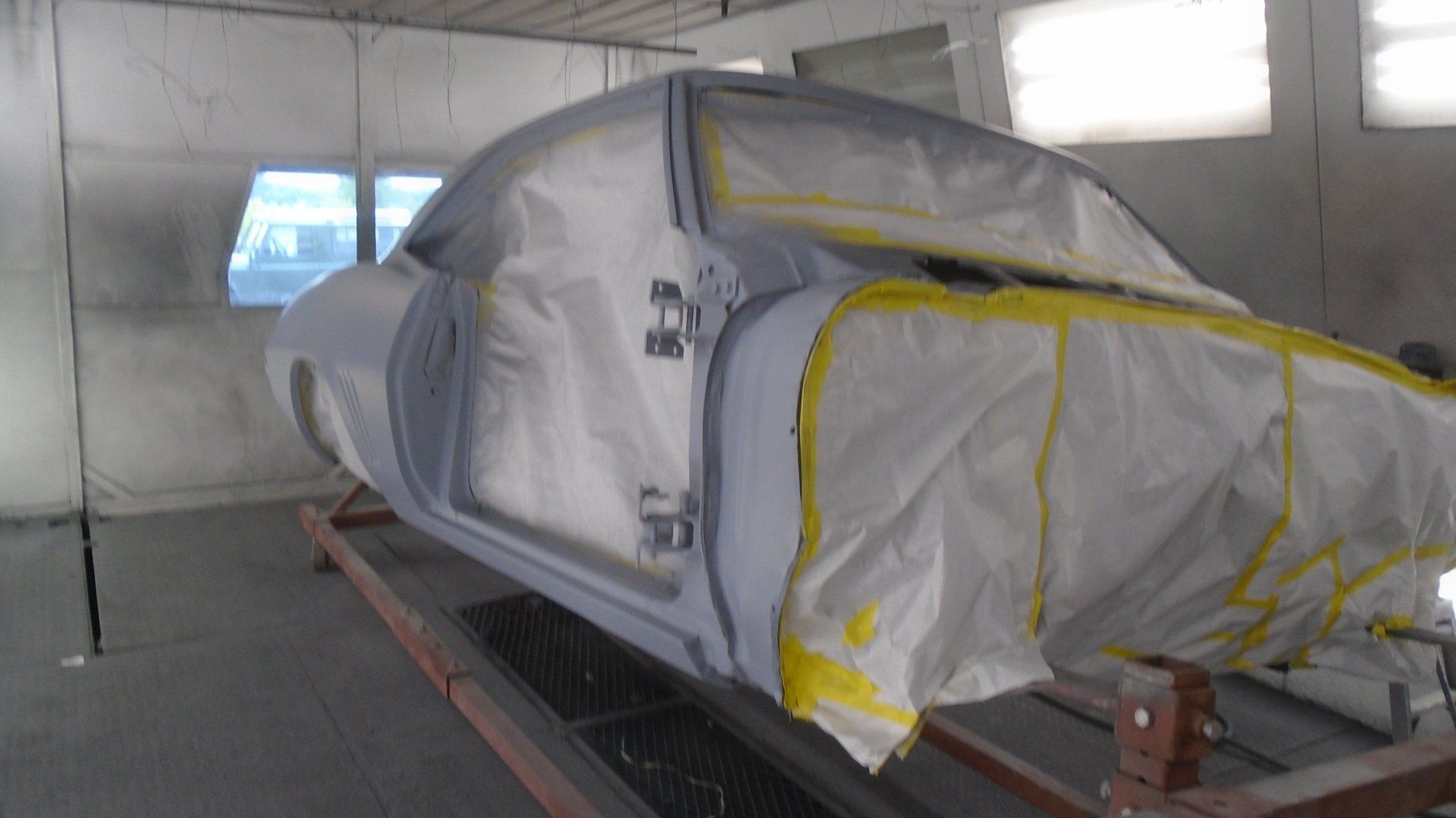 Car body masked for painting in a spray booth, with doors and windows covered in white plastic.