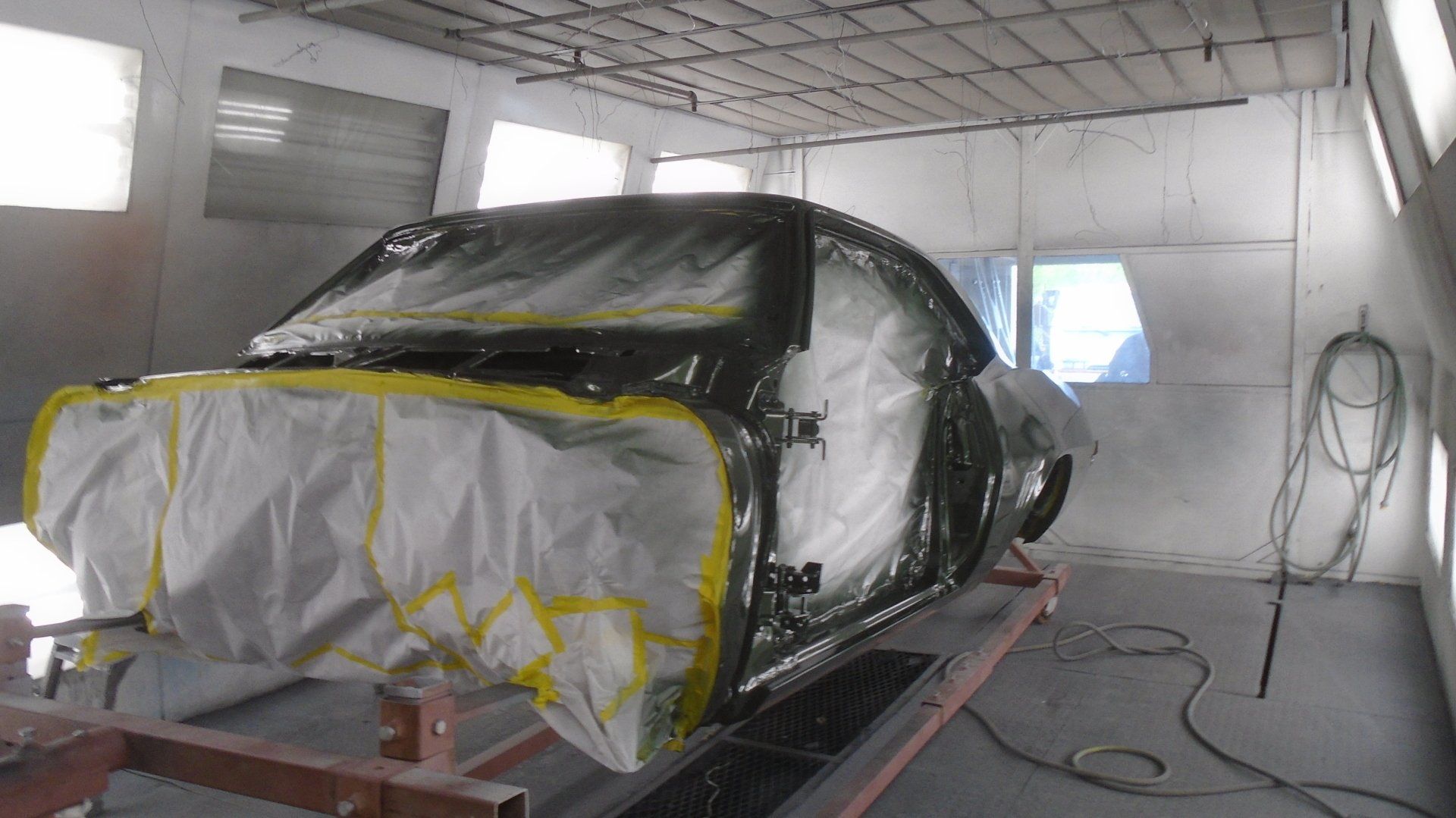 Car in a paint booth, covered in plastic and tape, ready for painting.