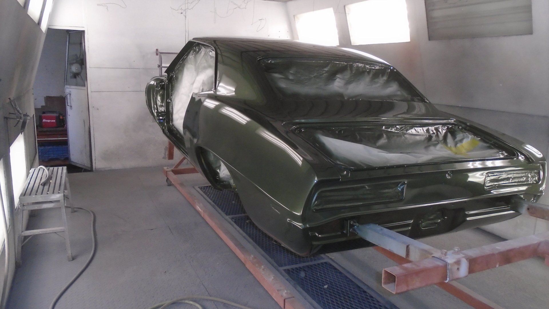 Dark green classic car in a paint booth being painted.