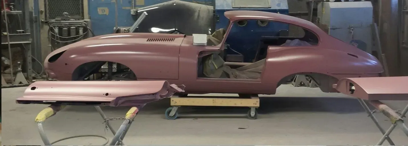 A car body in a workshop, partially assembled and painted pink. The door panels are separate.