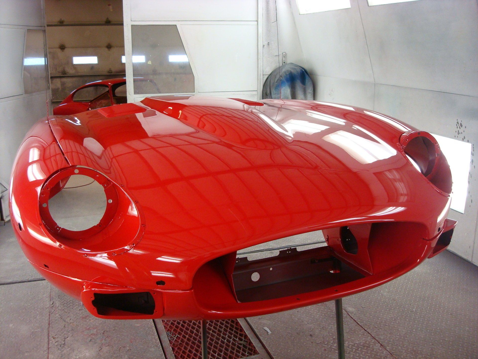 Red car front-end in a paint booth. Shiny finish with open headlight and engine bay.