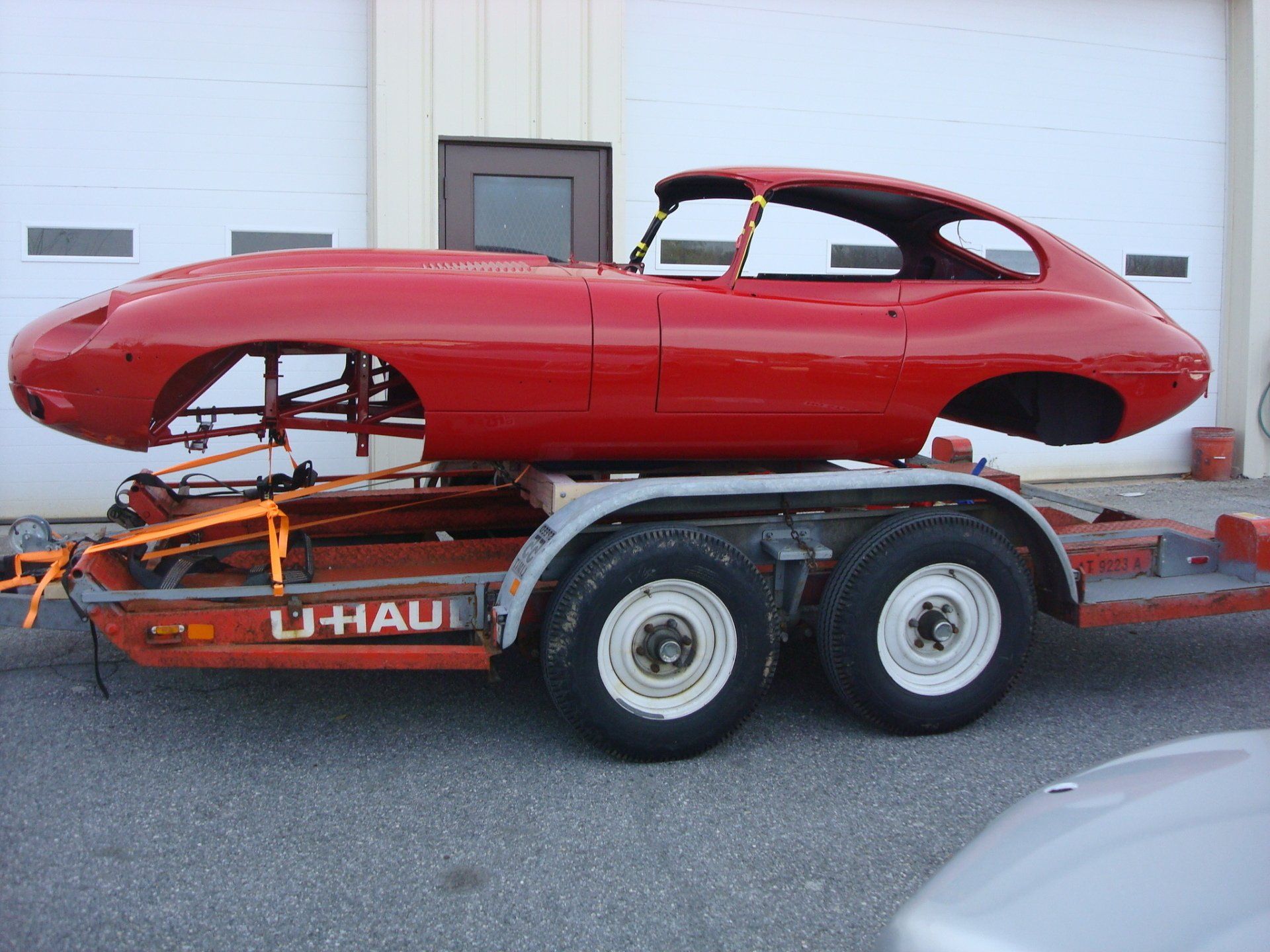 Red Jaguar E-Type car body on a U-Haul trailer.