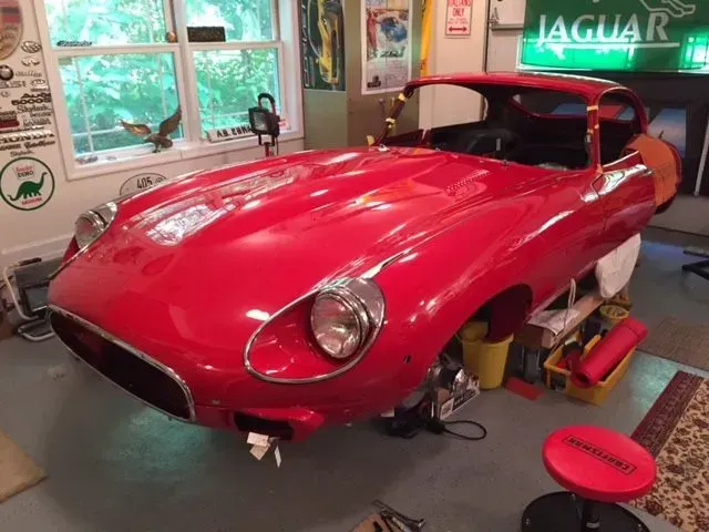 Red Jaguar E-Type car body in a garage, likely under restoration.