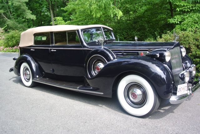 Black vintage Packard convertible with white-walled tires, parked on a paved road.