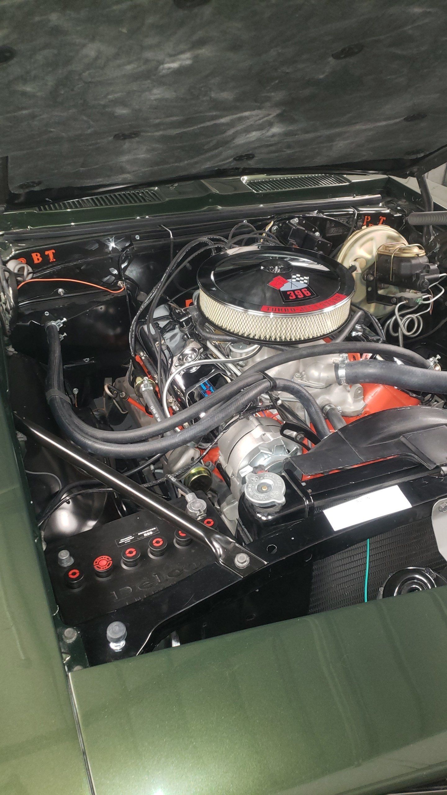 Green car engine bay with black components, air cleaner, and firewall insulation.