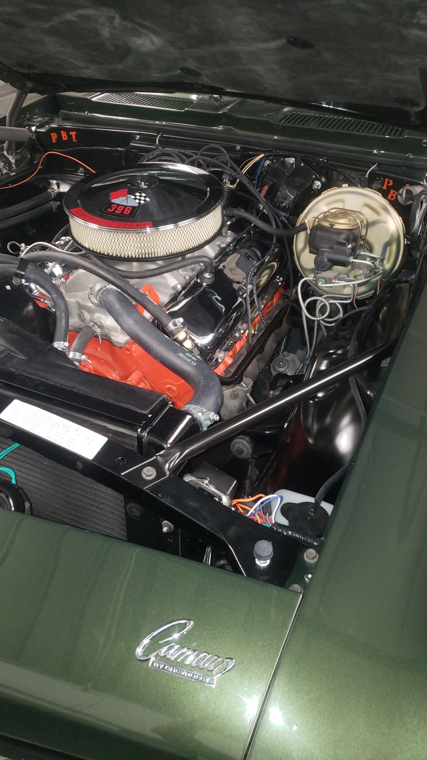 Green classic Camaro engine bay, chrome air filter, orange engine, black components, in a shop.