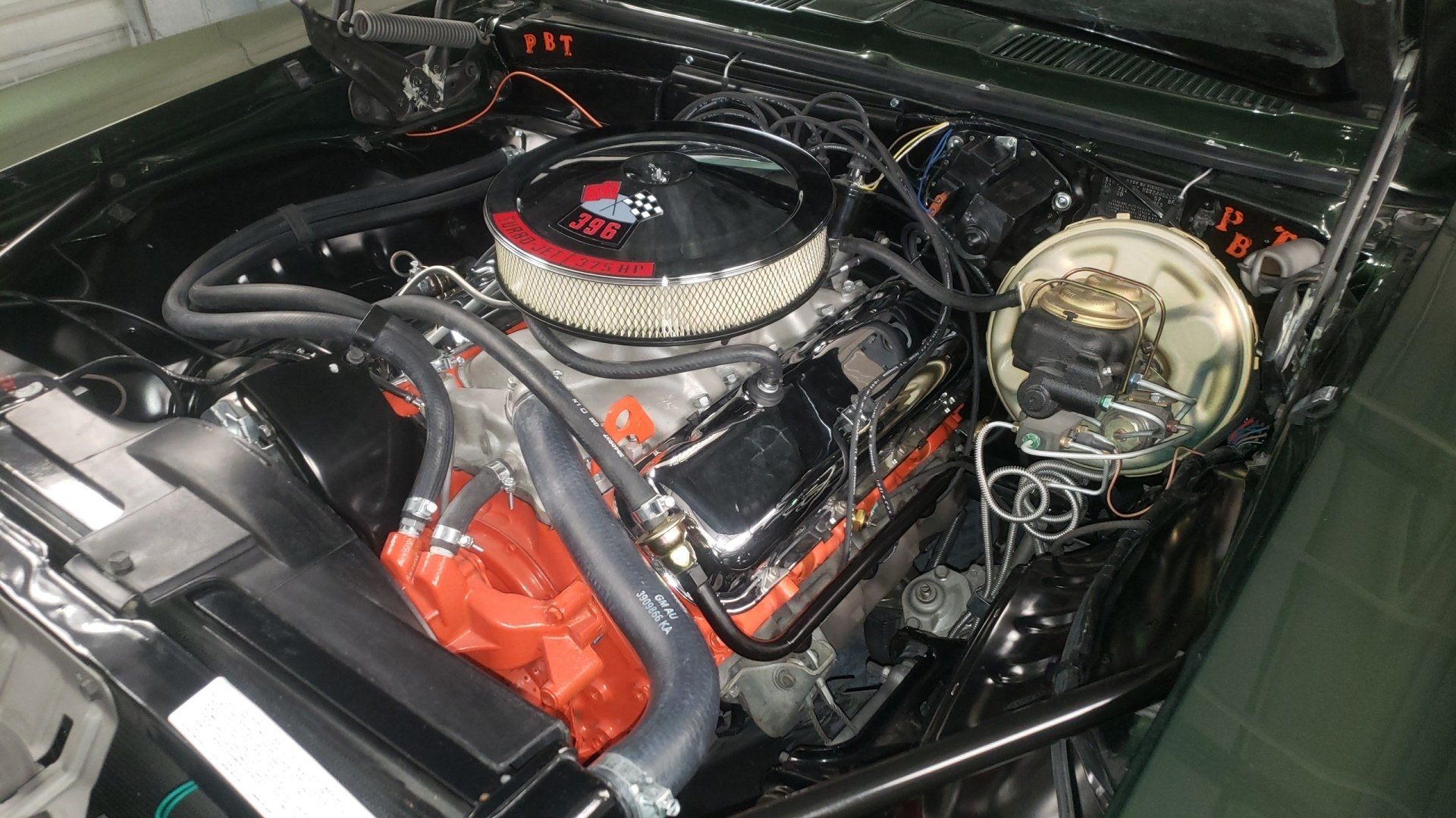 A classic green Chevrolet engine bay with a chrome air filter and orange engine components.