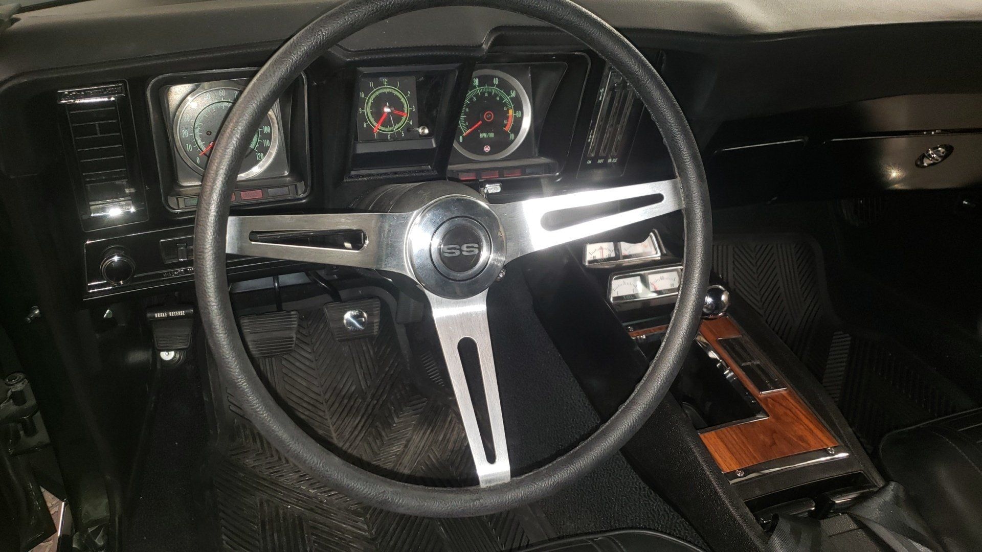 Black car interior with steering wheel, dashboard gauges, and wood trim console.