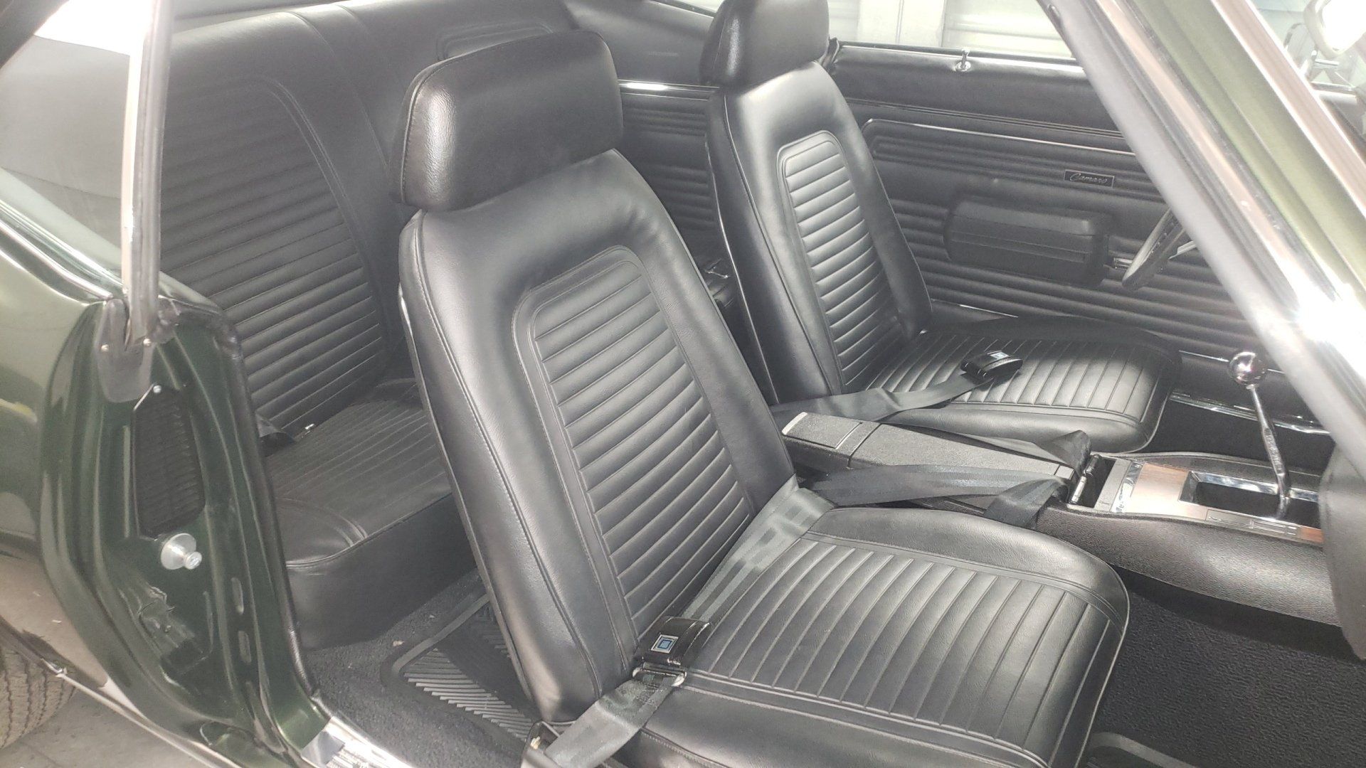 Black interior of a classic car, likely a Camaro. Features black seats, dashboard, and gear shift.