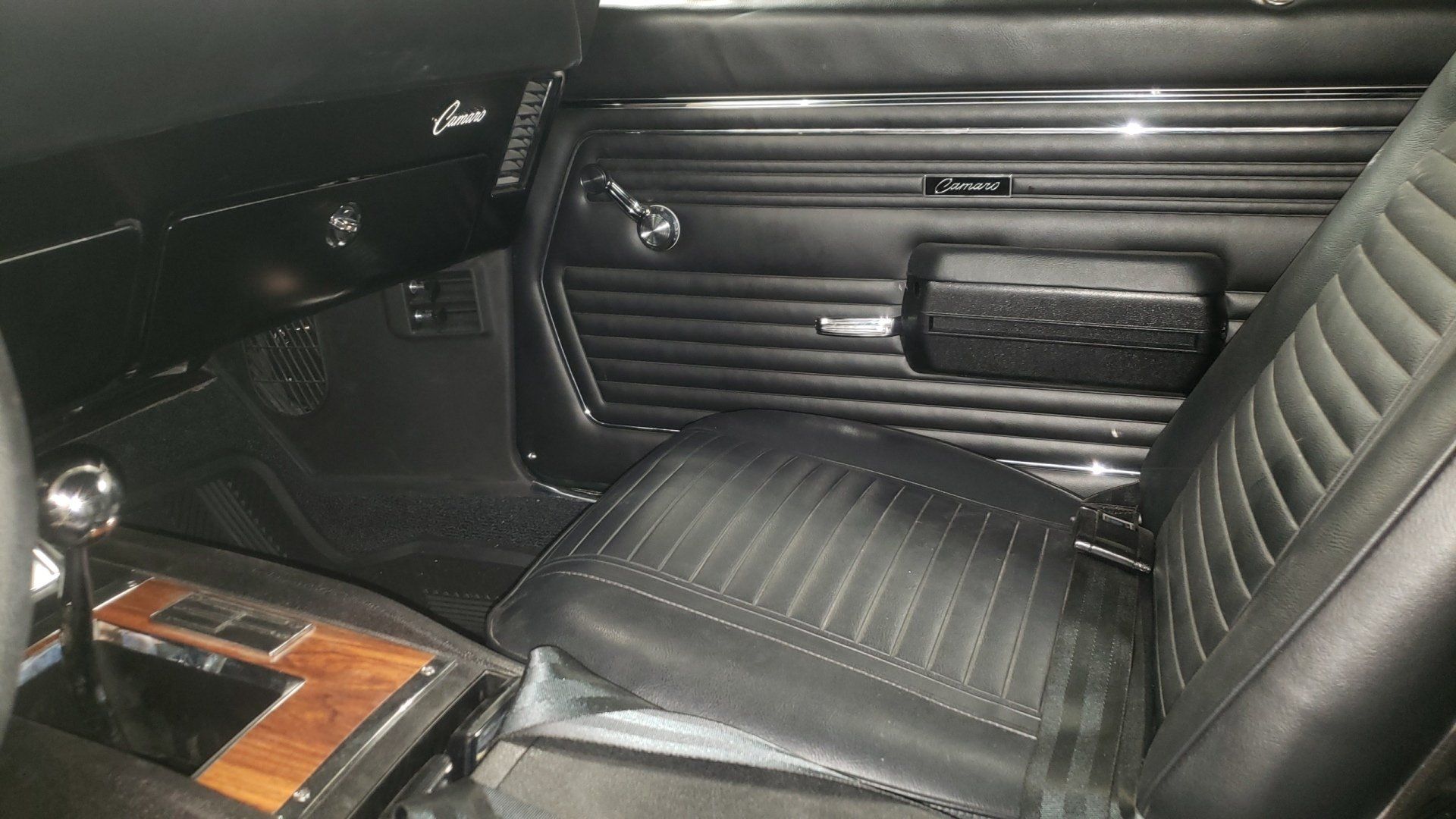 Black interior of a classic car, including a seat, door panel, and center console with a wooden accent.