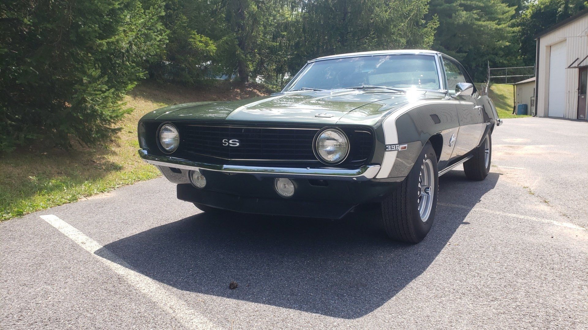 Green 1969 Chevrolet Camaro SS parked on asphalt, white racing stripe, black grill, sunny day.