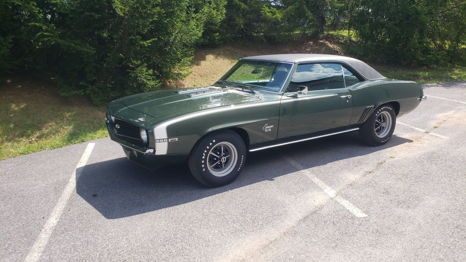 Green 1969 Chevrolet Camaro in a parking lot, with a black vinyl roof and white stripe.