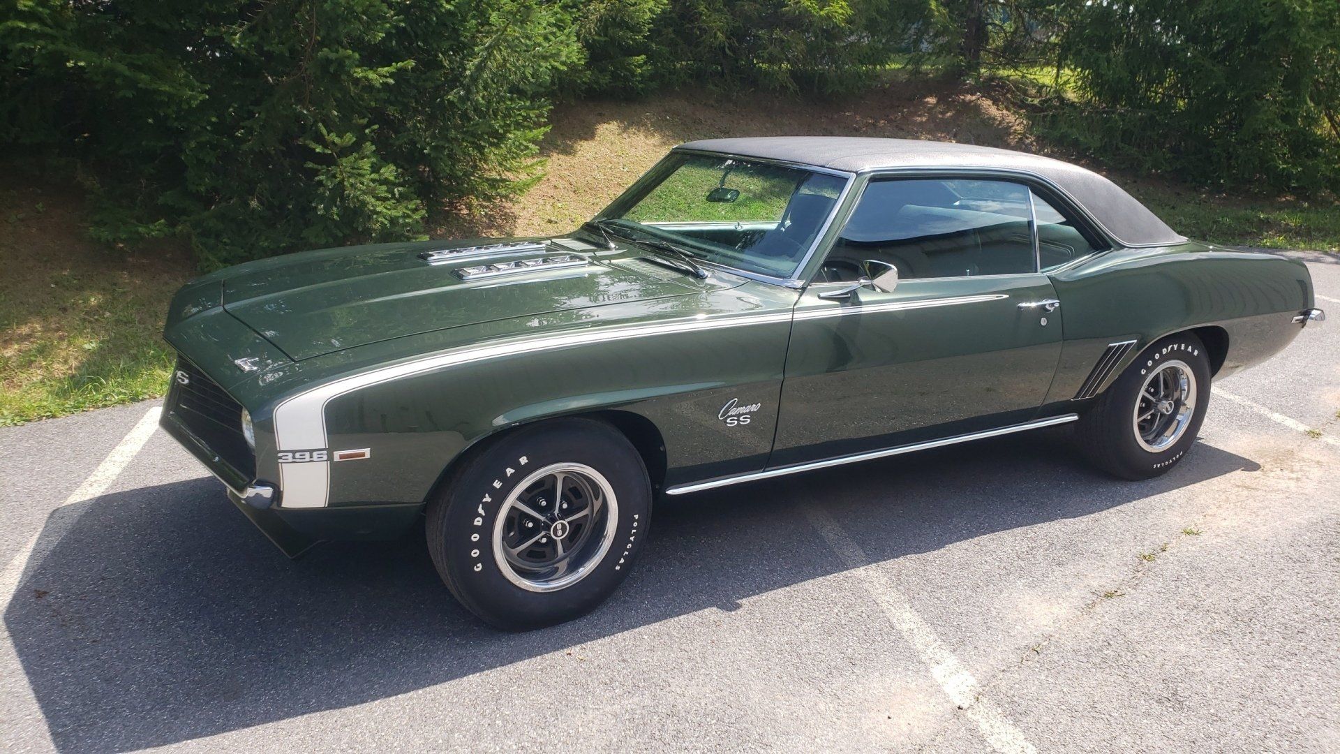 Dark green 1969 Chevrolet Camaro with gray roof, white stripe, black wheels, parked outdoors.