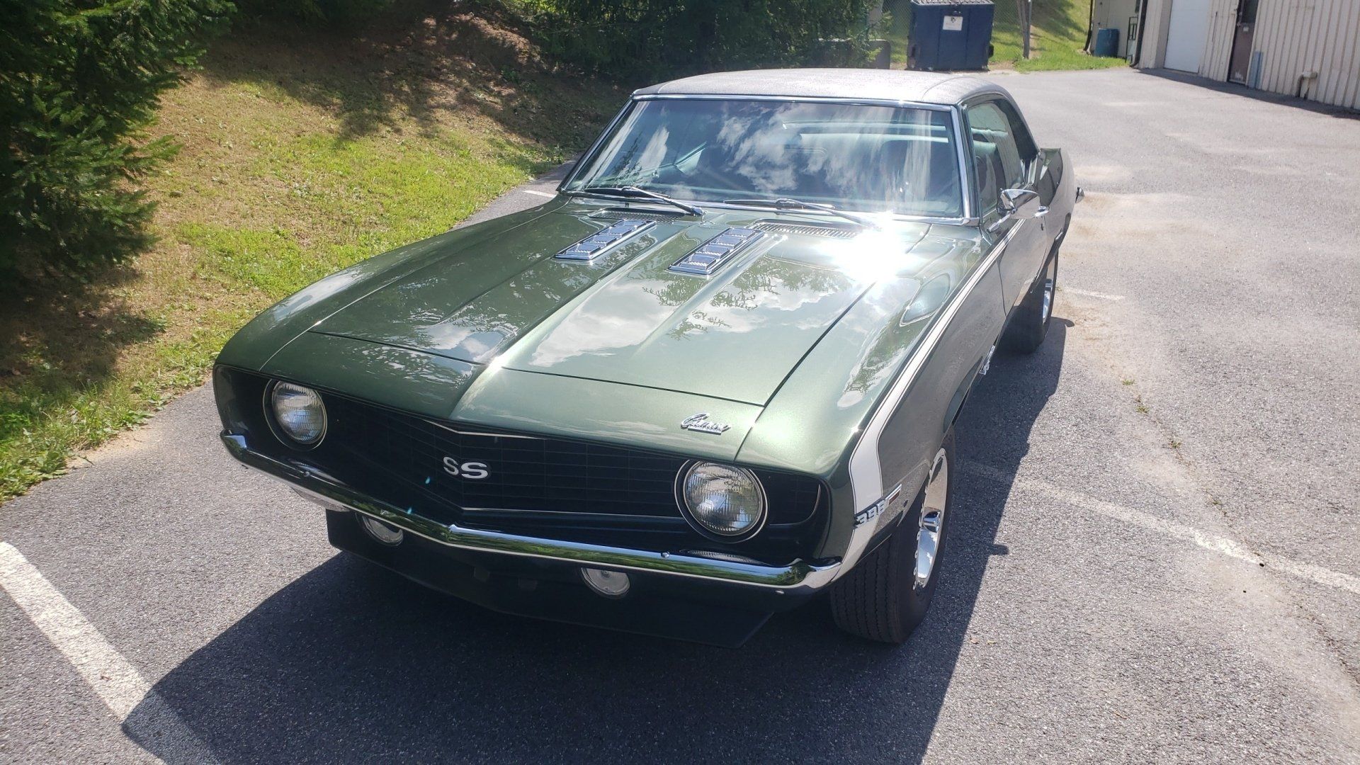 Green and white classic Chevrolet Camaro, parked on asphalt, sunny day.