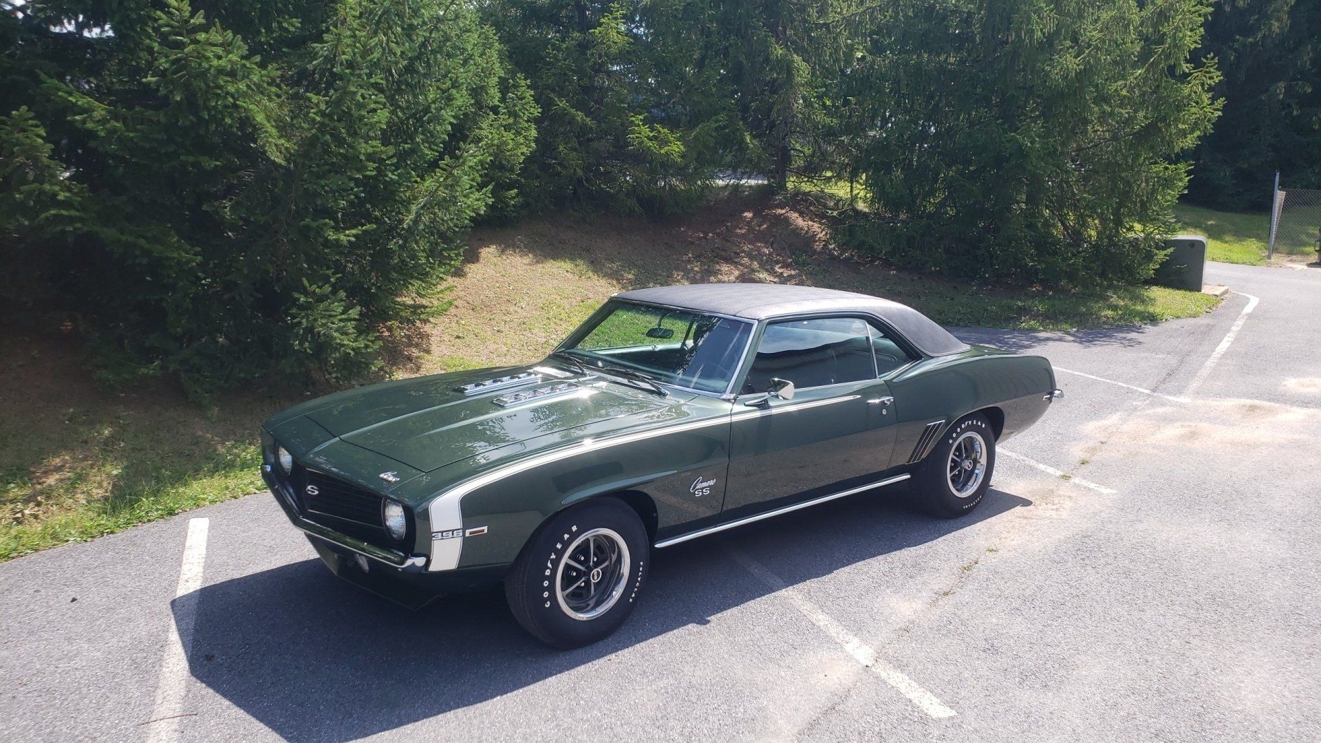 Green and silver 1969 Chevrolet Camaro SS parked on asphalt, trees in background.