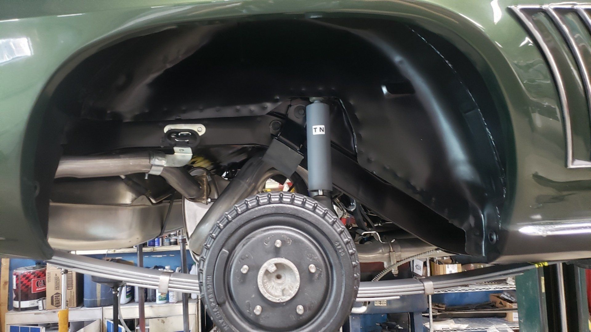 Green car's rear wheel and suspension detail. Black painted components, tire, and exhaust visible.