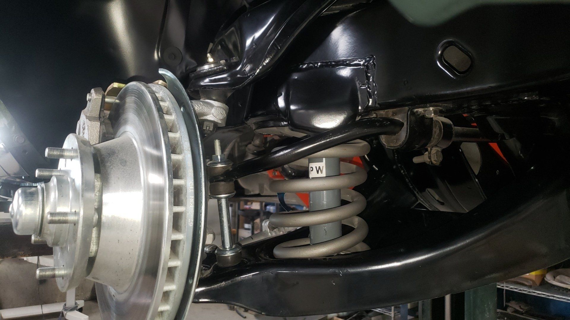 Close-up of a car's front suspension system, showcasing the brake rotor, spring, and control arms against a black frame.