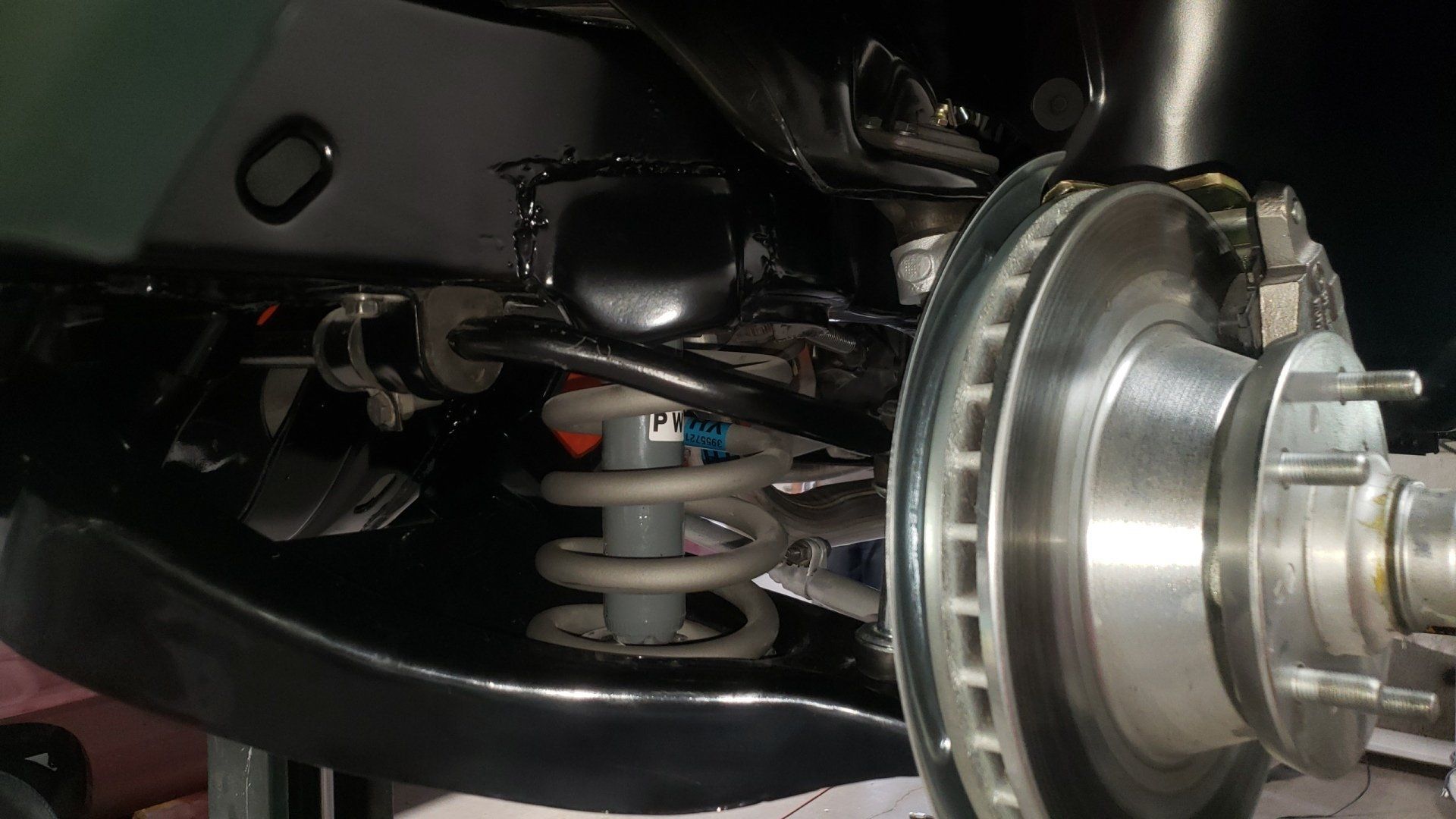 Close-up of a car's front suspension with a coil spring, shock absorber, and brake rotor visible.