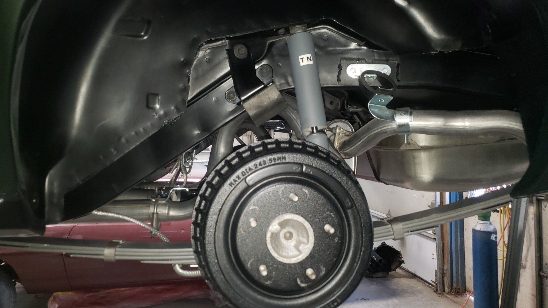 Black car's rear suspension, tire, and wheel well viewed from underneath. Exhaust pipe and shock absorber visible.