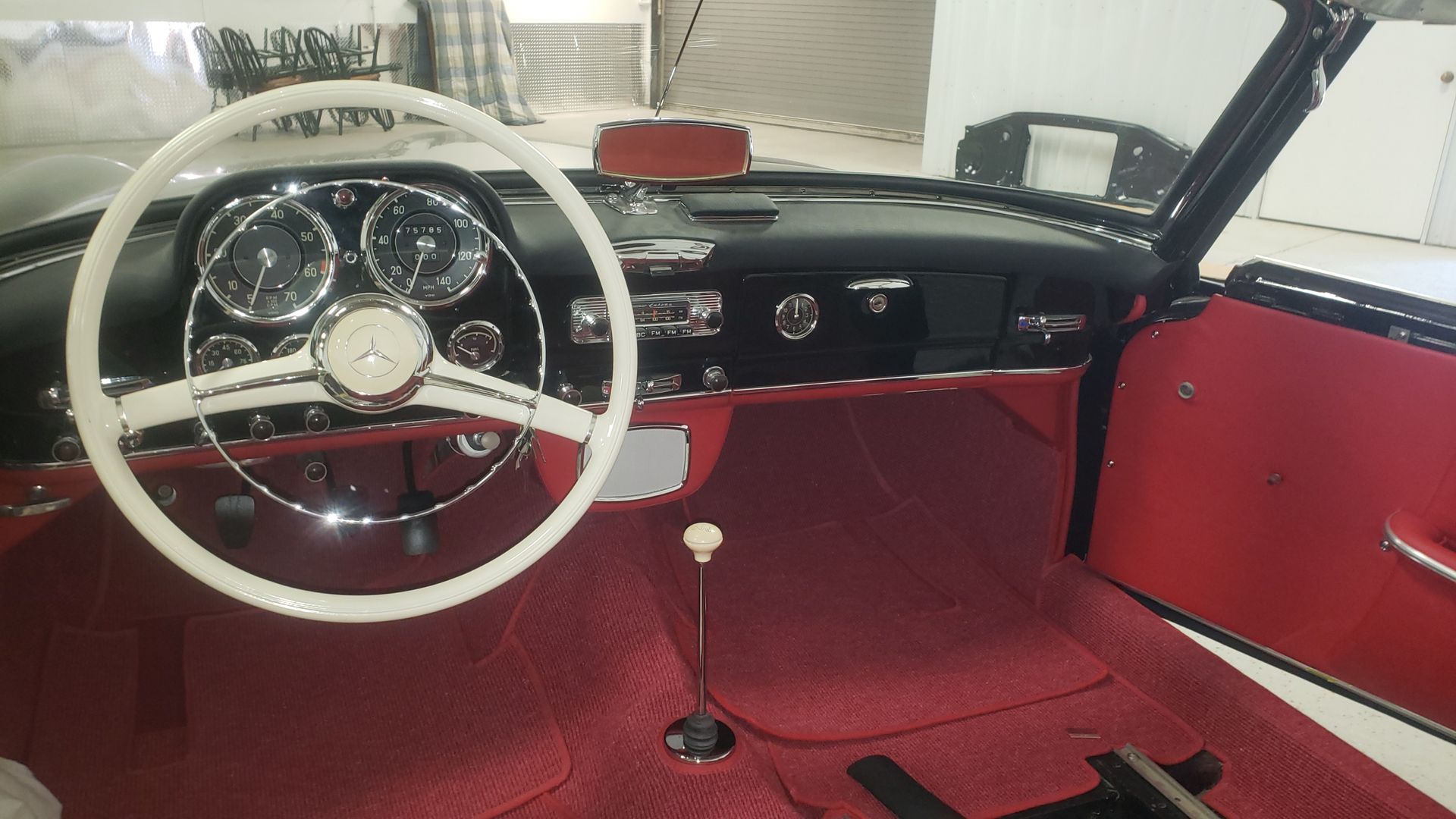 Interior of a classic Mercedes-Benz convertible; red upholstery, white steering wheel, black dashboard.
