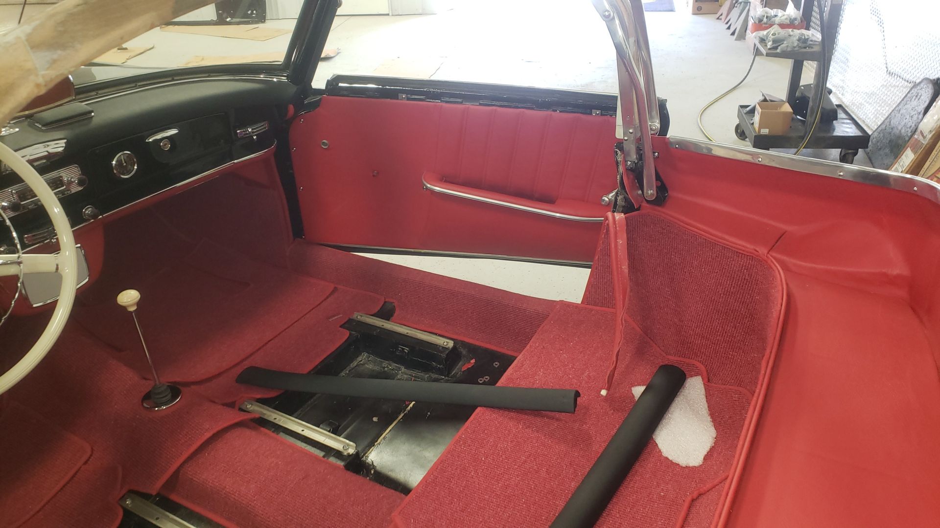 Red interior of a classic car, with a white steering wheel and black accents.
