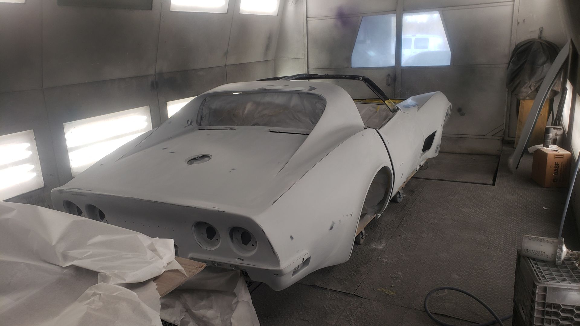 A white classic Corvette undergoing restoration inside a paint booth.