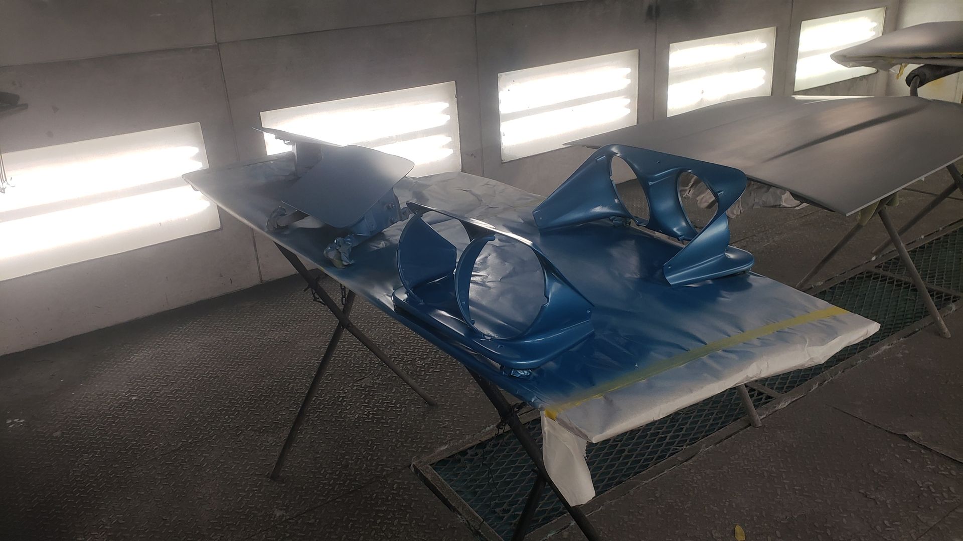 Blue car parts on a table in a paint booth.