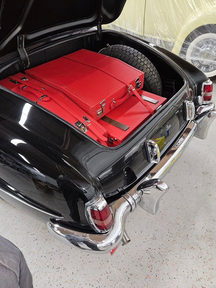 Black classic car trunk with red luggage and spare tire.