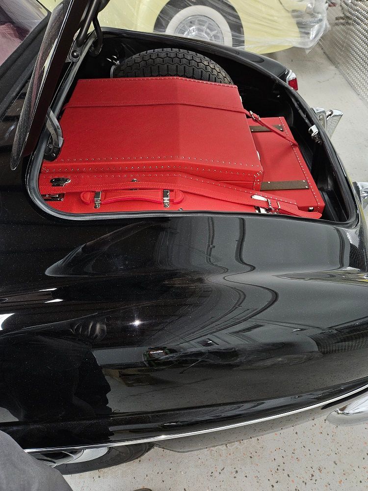 Black vintage car trunk open, filled with red luggage and spare tire.