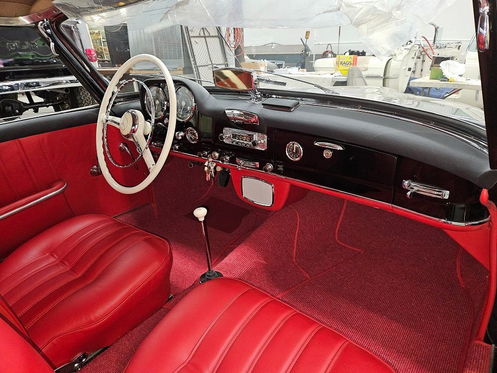 Interior of a classic car with red seats, black dashboard, and white steering wheel.