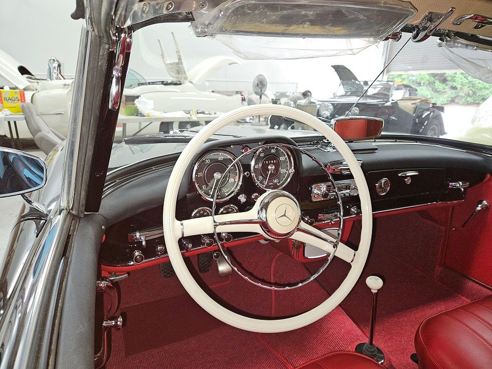 Interior view of a classic Mercedes-Benz car with white steering wheel, red interior, and chrome accents.