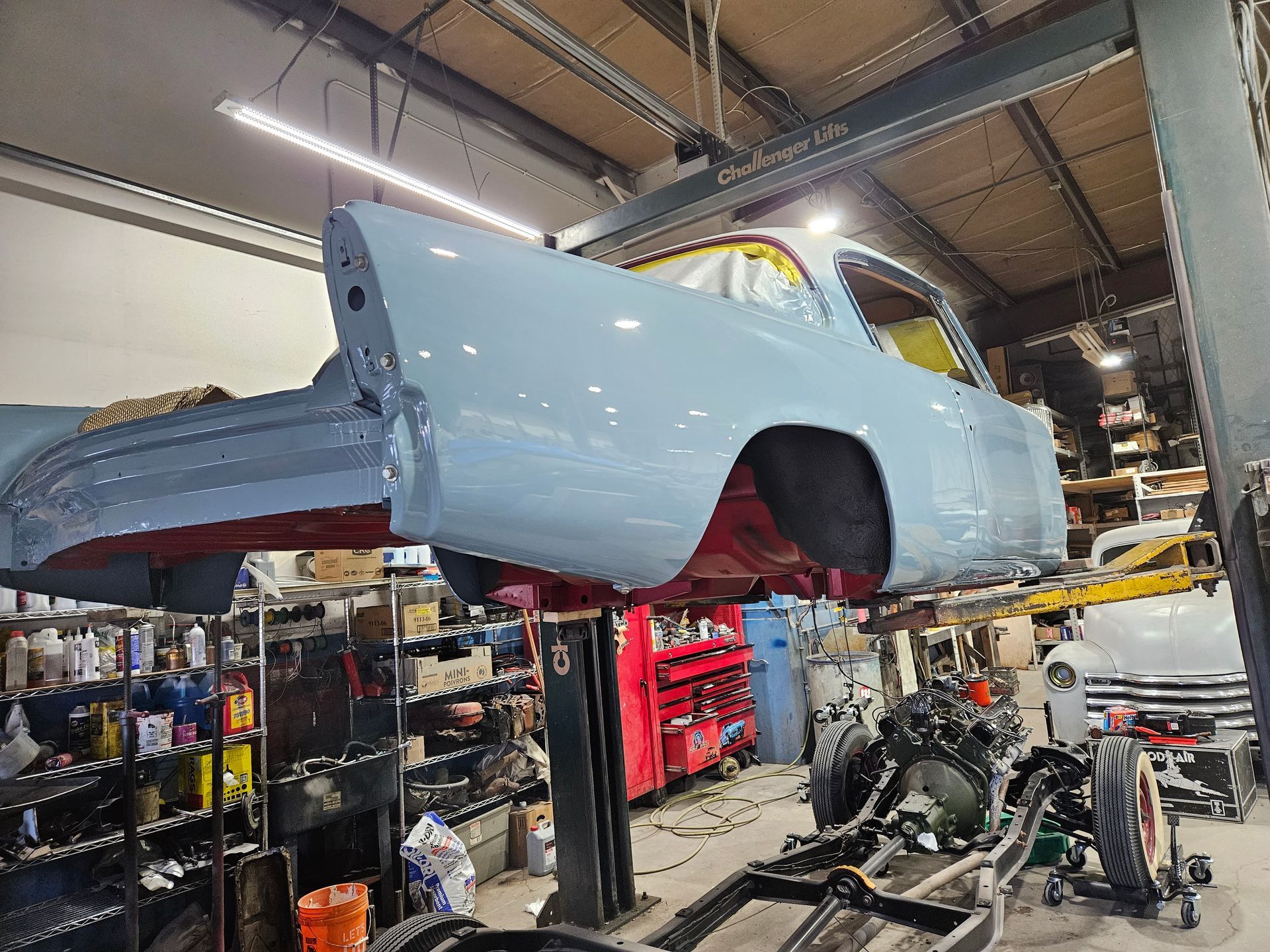 Classic light blue car body on a lift in a workshop, undergoing restoration.