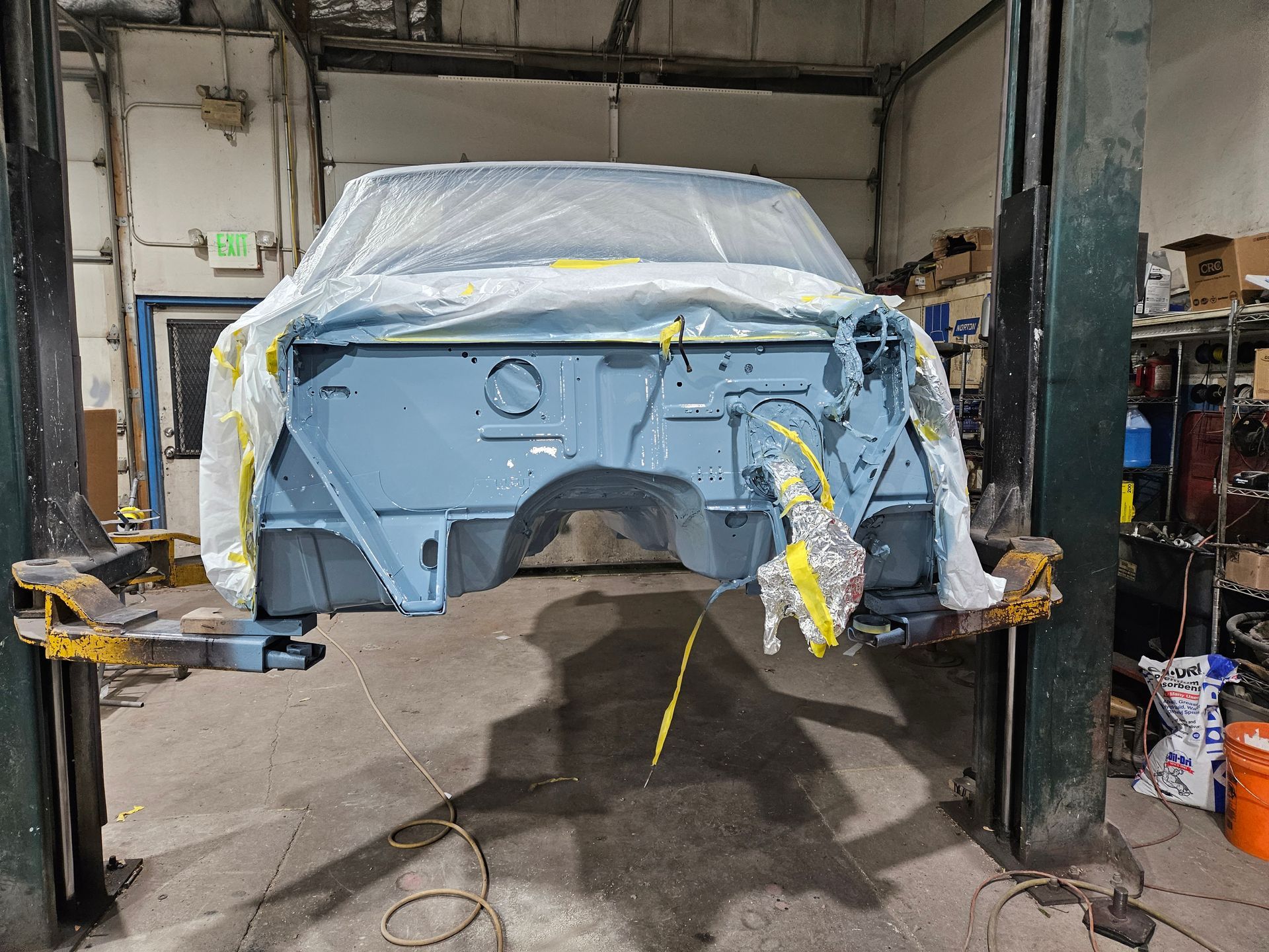 Blue truck body in a shop, on a lift, covered in plastic, ready for paint.