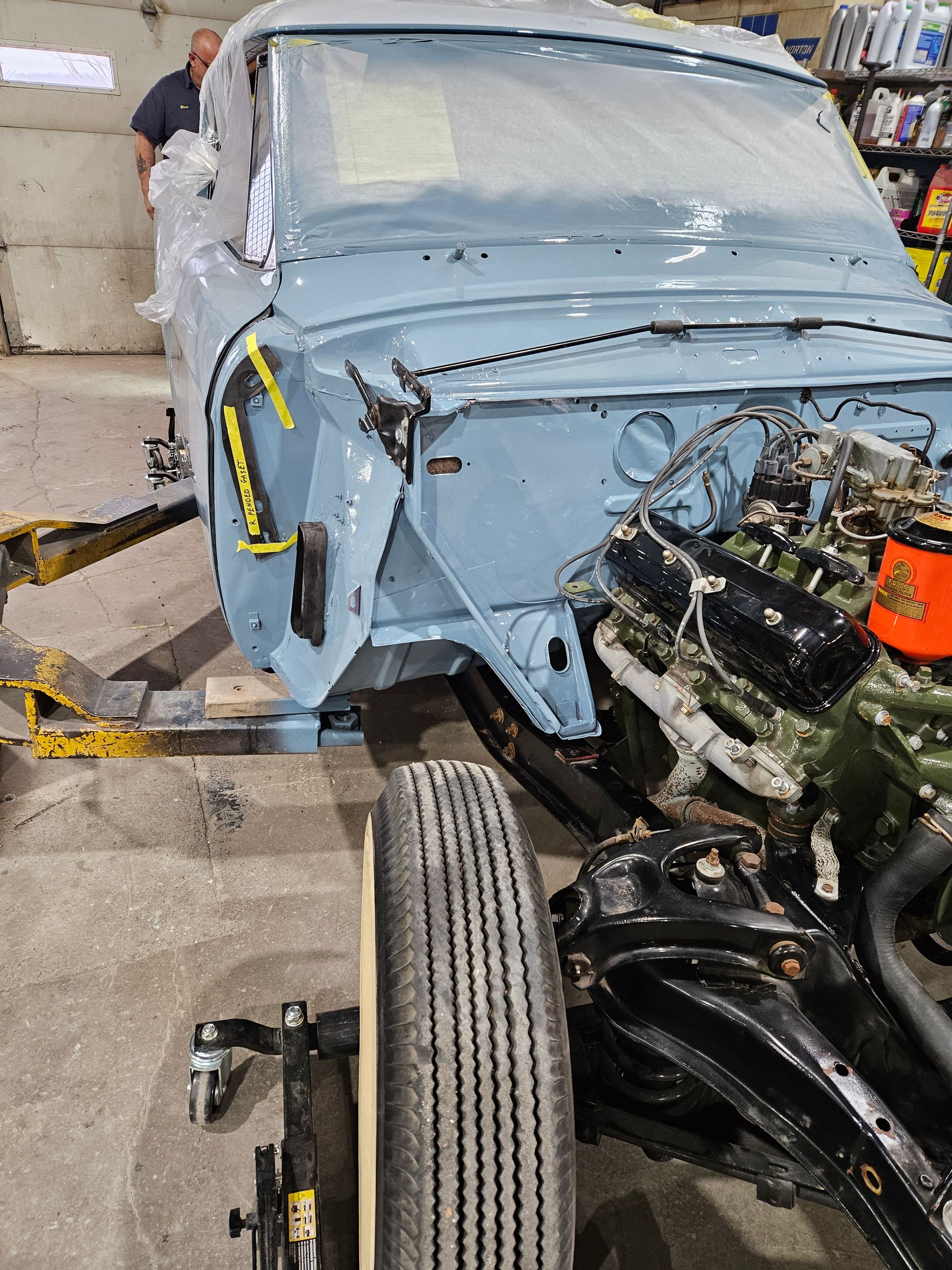 Light blue classic car in restoration, with exposed engine and tire. Man in background.