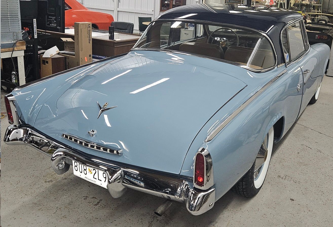 Light blue and dark blue classic Studebaker car with white-wall tires, in a workshop setting.