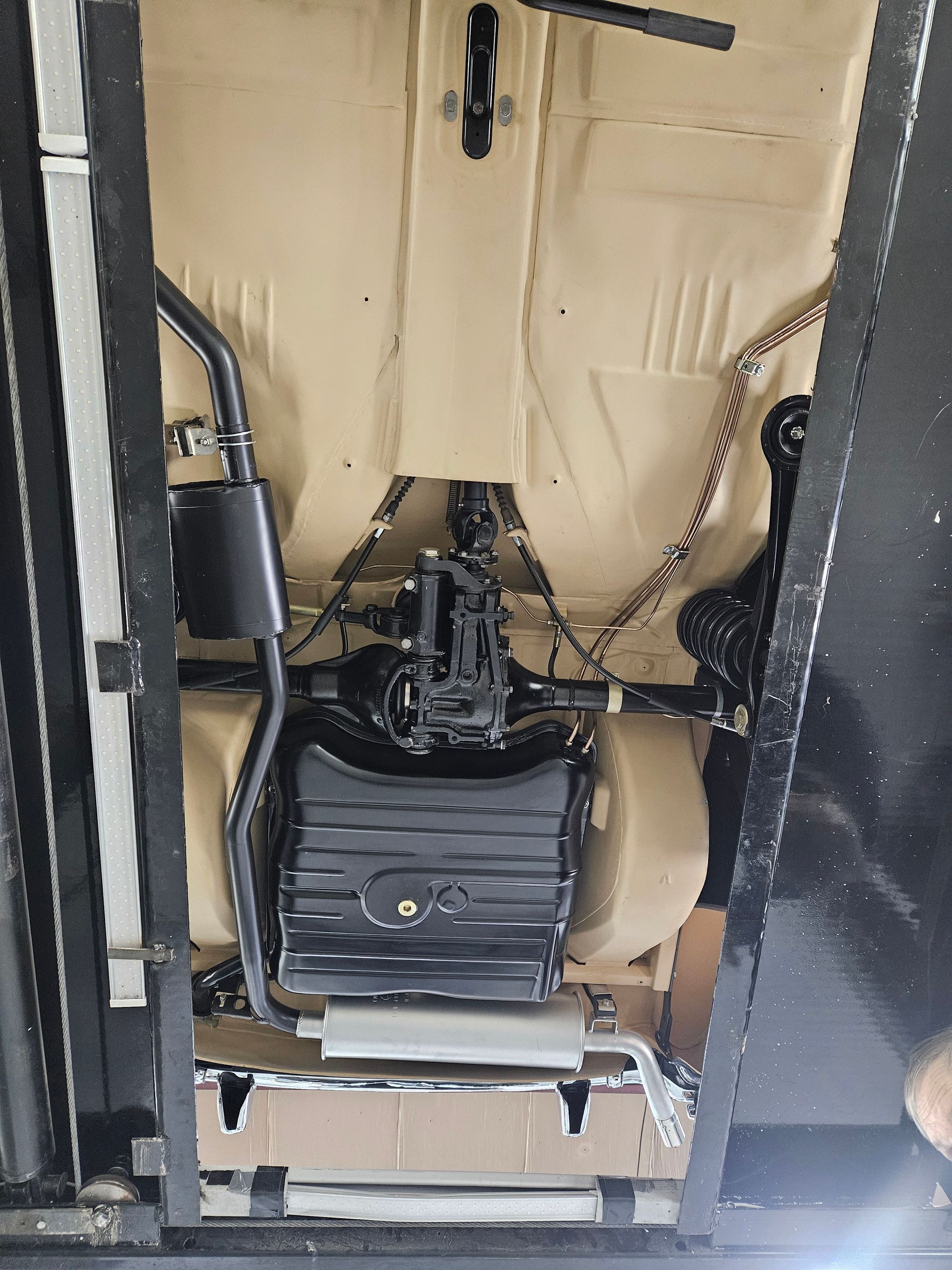 Underside of a car in a lift, showing beige floor, black exhaust and suspension components.