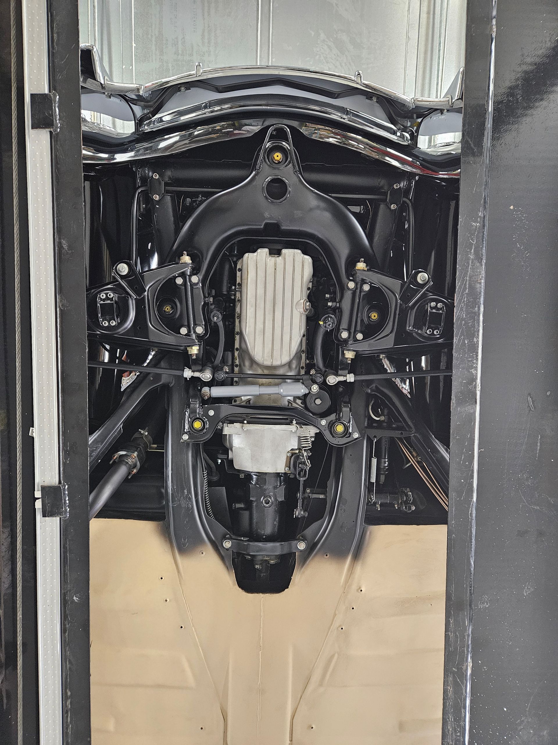 Underside of a black car, showing suspension and engine components, viewed from below in a garage setting.