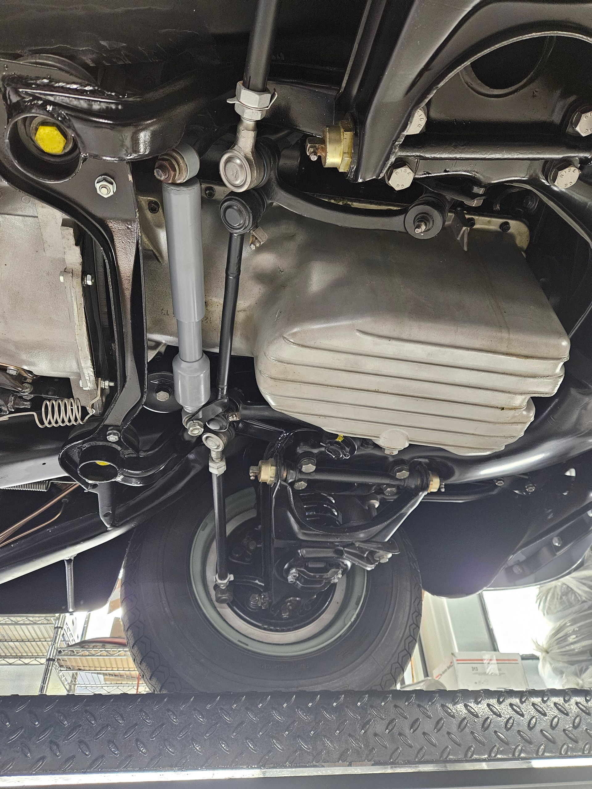 Underside of a car on a lift; visible wheel, suspension, and engine components; black and silver colors.