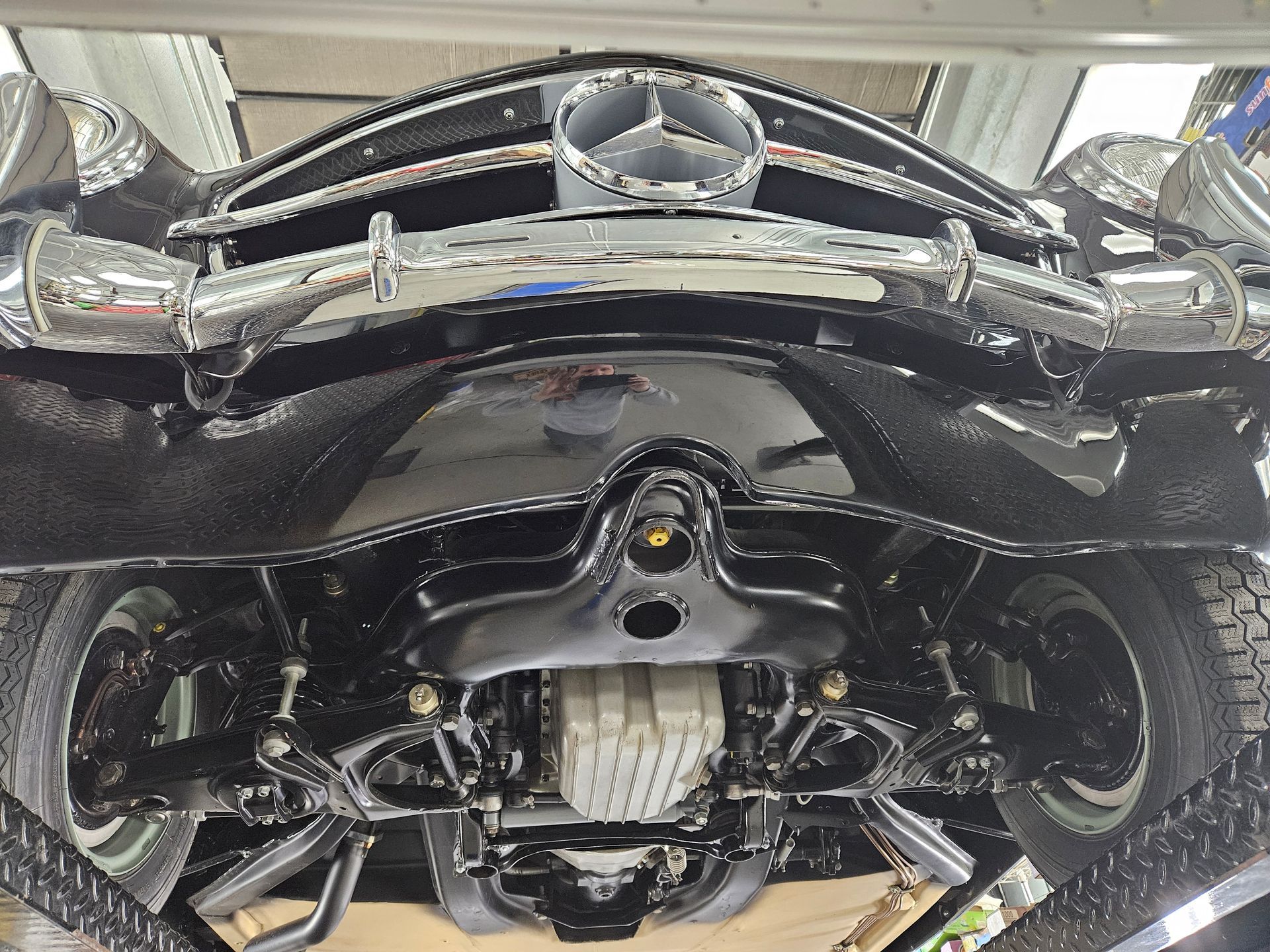 Undercarriage view of a restored black Mercedes-Benz classic car, showing detailed components and shiny chrome.