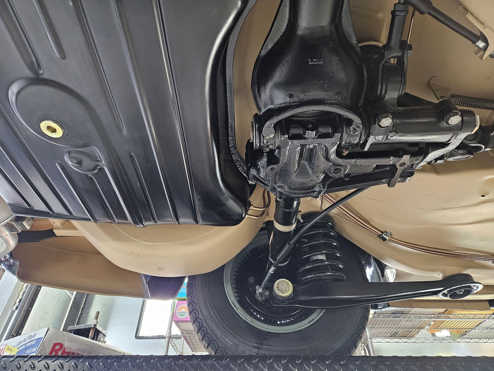 Underside of a beige car showcasing rear suspension, fuel tank, and a black painted differential.